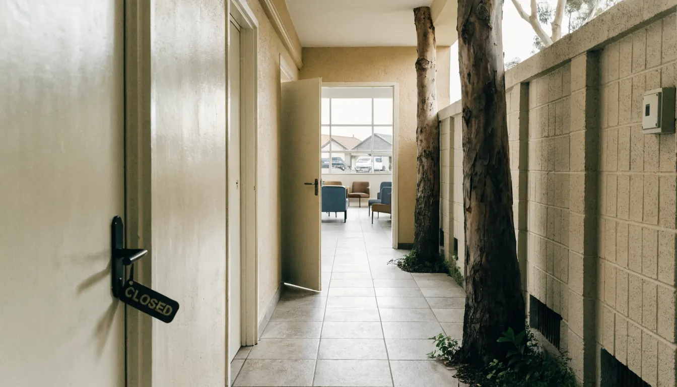 A closed corridor door beside an open one leading to a softly lit waiting room